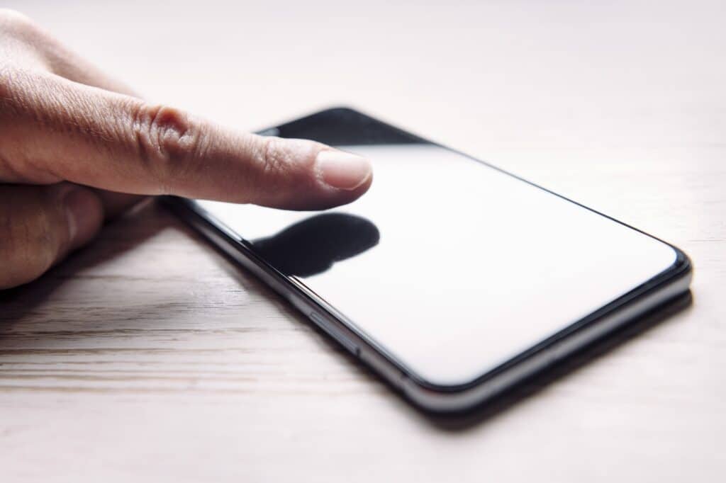 finger touching the screen of a phone on table